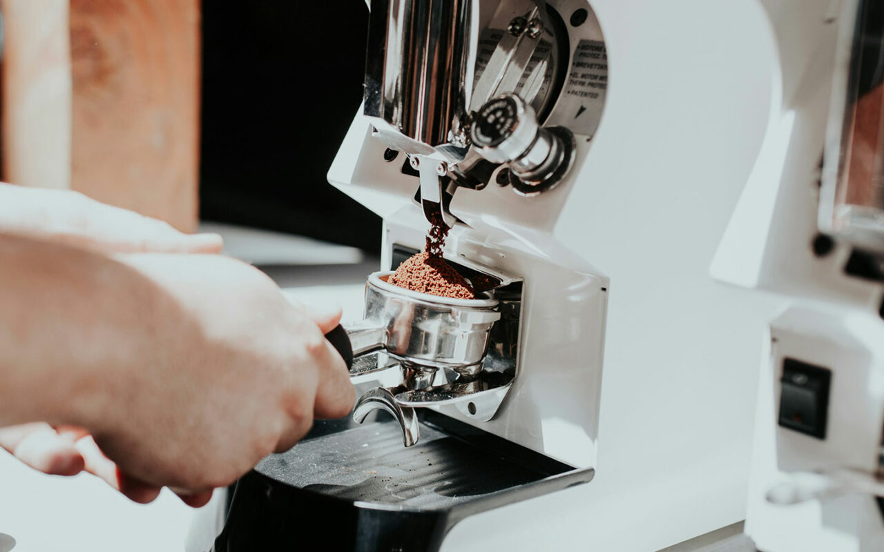 Une personne utilise une machine à moudre du café pour remplir un porte-filtre avec du café fraîchement moulu, préparant une dose pour un expresso.