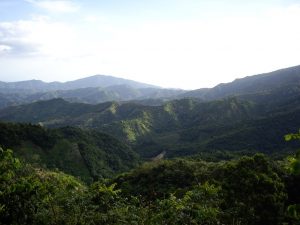 Vue panoramique des montagnes de la Sierra Maestra, avec des collines verdoyantes sous un ciel clair.