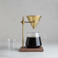 Carafe Kinto SCS 600 ml utilisée dans un ensemble pour café filtre avec un cône métallique doré sur un support en bois.