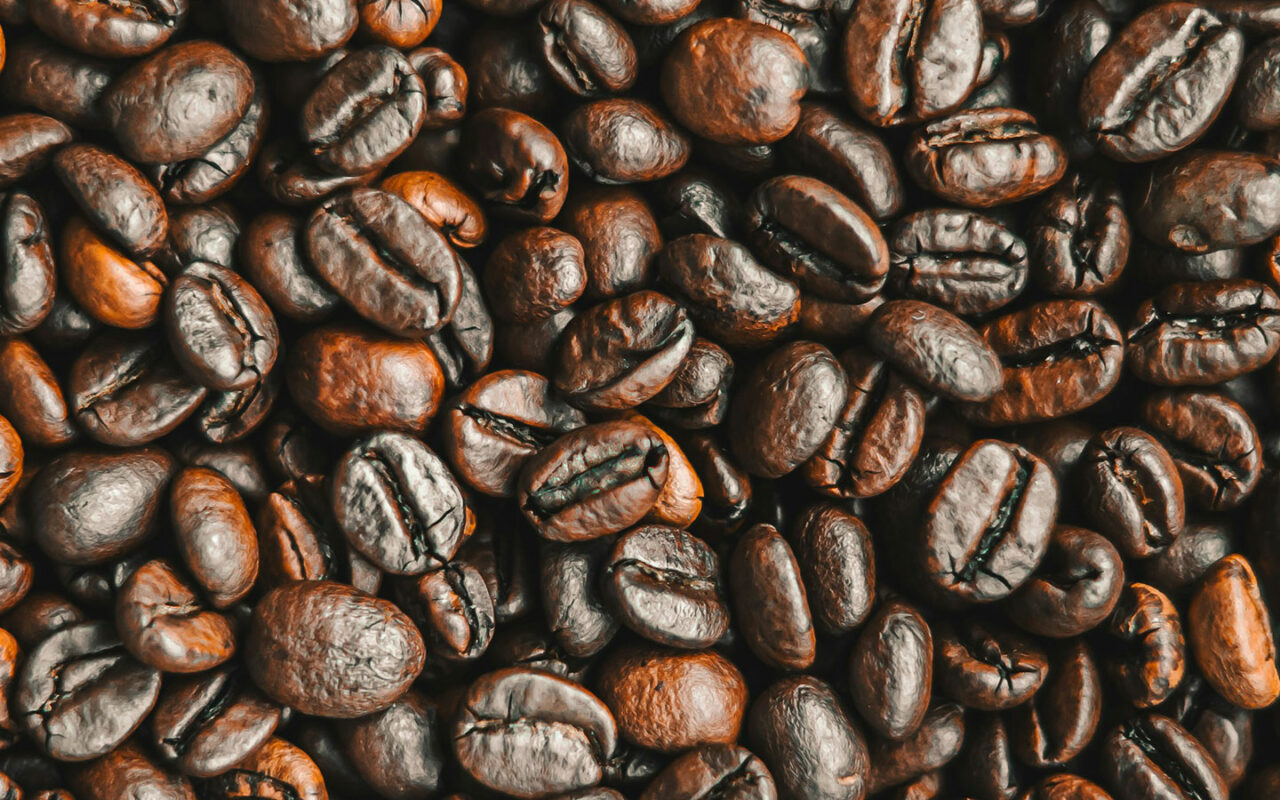 Gros plan sur des grains de café torréfiés dans un style de torréfaction foncée, montrant leur couleur brun très foncé avec une légère brillance en surface. Les grains sont empilés de manière dense, mettant en valeur leur texture lisse et uniformément torréfiée.