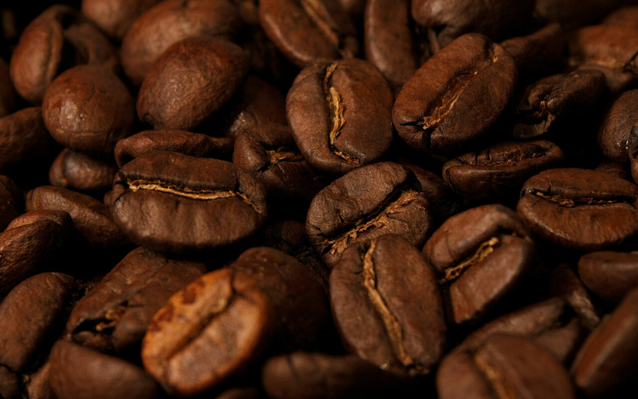 Gros plan sur des grains de café torréfiés dans un style de torréfaction medium, montrant leur couleur brun moyen et les détails de leurs fissures naturelles. Les grains sont disposés en une masse dense, créant une texture riche et uniforme.