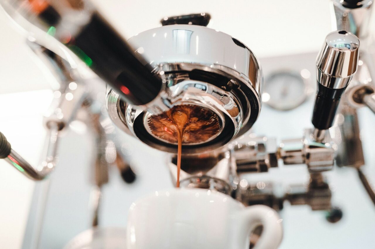 Gros plan sur une machine à espresso en acier inoxydable, en train d'extraire du café qui coule dans une tasse blanche en dessous. Les détails chromés de la machine brillent, mettant en valeur la précision du processus d'extraction.