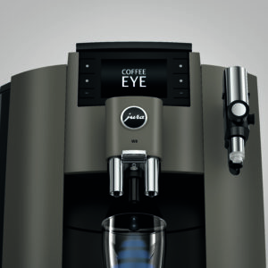 Une machine à café Jura W8 vue de face avec un affichage numérique indiquant "COFFEE EYE". La machine est de couleur noire et grise, avec des boutons et un bec verseur central sous le logo "Jura"