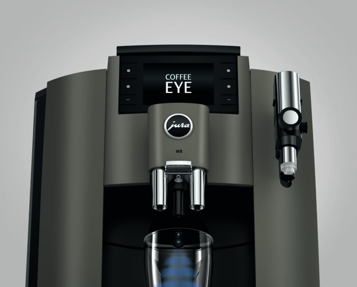 Une machine à café Jura W8 vue de face avec un affichage numérique indiquant "COFFEE EYE". La machine est de couleur noire et grise, avec des boutons et un bec verseur central sous le logo "Jura"