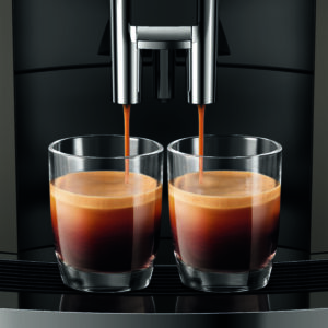 Deux verres se remplissent simultanément d'espresso à partir du bec verseur d'une machine à café Jura W8, montrant le processus d'extraction avec une crème épaisse sur le café.