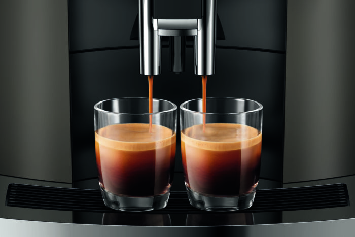 Deux verres se remplissent simultanément d'espresso à partir du bec verseur d'une machine à café Jura W8, montrant le processus d'extraction avec une crème épaisse sur le café.