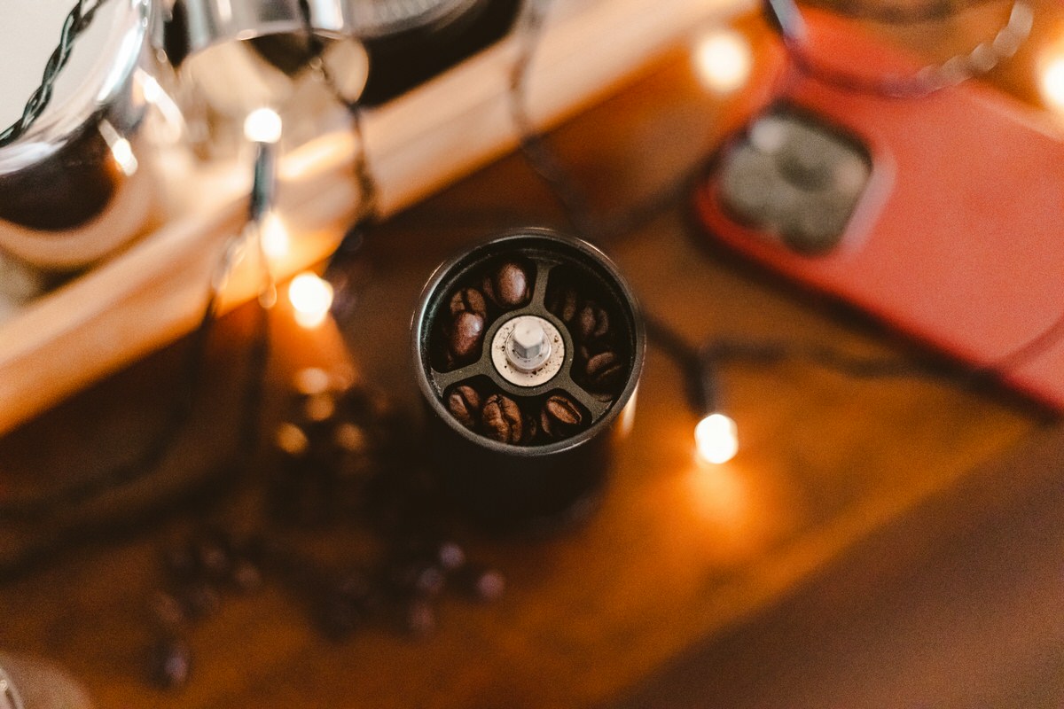 Vue rapprochée d’un moulin manuel rempli de grains de café, entouré d’une ambiance chaleureuse avec des lumières douces.